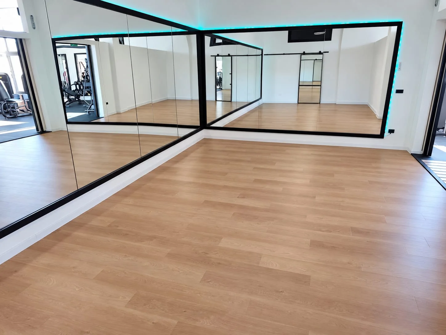 Seconda vista della sala corsi con pavimento in legno e pareti a specchio